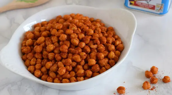 Un tazón blanco lleno de garbanzos fritos crujientes, sazonados con especias rojizas.