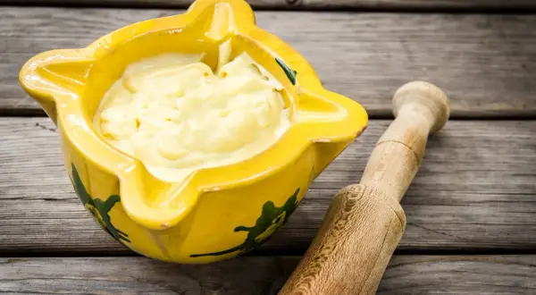 Alioli cremoso en mortero amarillo, listo para tu receta.