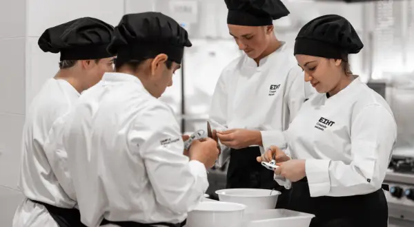 Estudiantes en cursos de cocina para profesionales, concentrados en sus tareas en una cocina profesional.