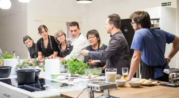 Grupo de personas aprendiendo en un curso de cocina mediterránea. Ingredientes frescos y utensilios listos para cocinar.