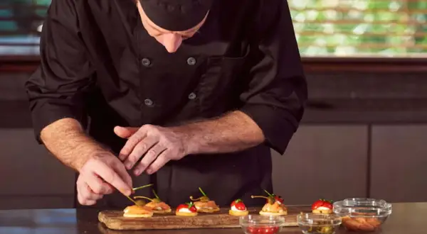 Chef en uniforme negro prepara canapés con salmón y alcaparras. Cada detalle cuenta en este arte de metre de cocina.