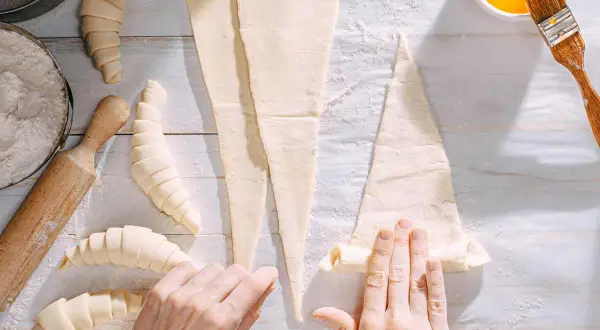 Manos enrollando masa para croissants. ¡Se pueden congelar los croissants para hornearlos más tarde!