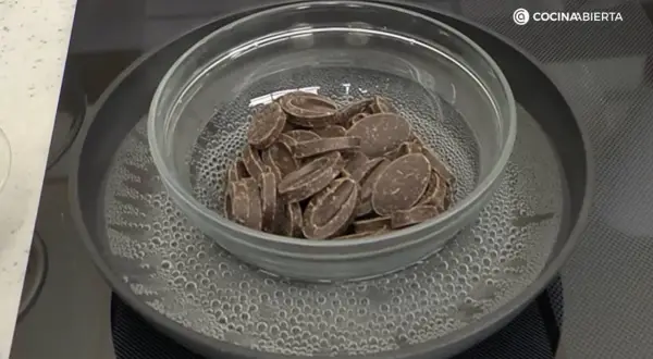 Chocolate troceado derritiéndose suavemente en un bol de cristal sobre un baño maría hirviendo.