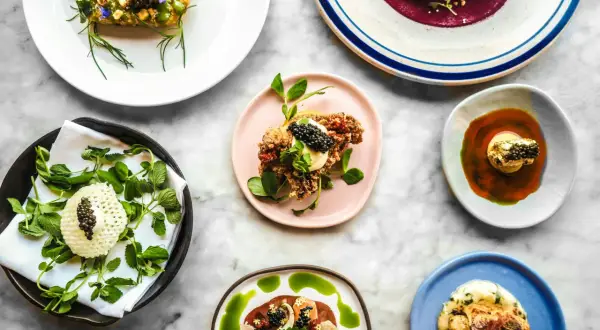 Deliciosos platos de un menú degustación, con caviar, flores comestibles y salsas vibrantes, presentados sobre una mesa de mármol.