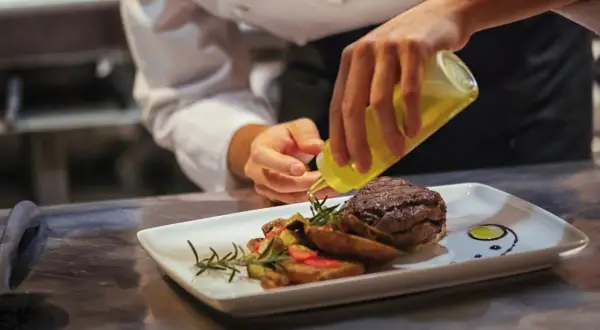 Chef finaliza plato de carne con guarnición. ¿Cuánto gana un cocinero en España? La pasión por la cocina se refleja en cada detalle.