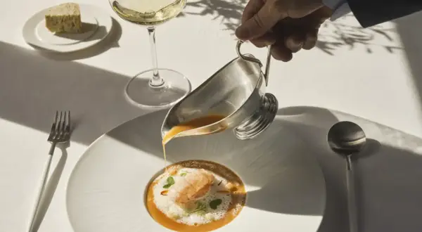 Servicio de sopa de marisco en un restaurante estrella Michelin. Un camarero vierte el caldo sobre un langostino y espuma.