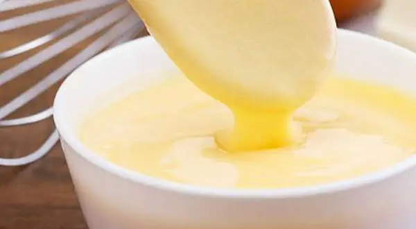 Crema pastelera cremosa cayendo de una cuchara a un bol. ¡Es bueno saber que se puede congelar la crema pastelera para usarla más tarde!