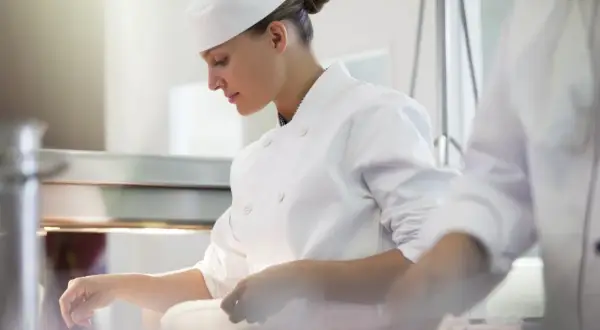 Chef concentrada en su labor, junto a otro chef en la cocina.