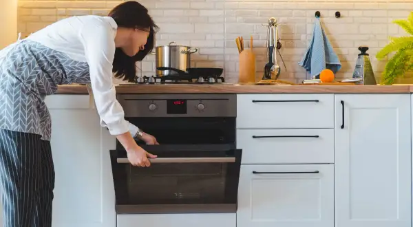 Mujer abre horno para cocinar al vapor en horno convencional.
