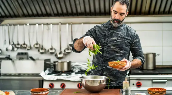 Chef con barba añade hierbas a un bol. Su trabajo en la direccion de cocina FP es impecable.