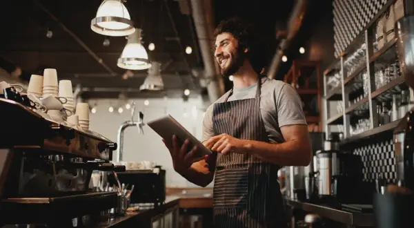 Gerente de un restaurante revisa pedidos en su tableta, sonriendo.