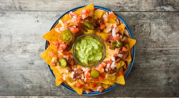 Nachos con queso derretido, carne, tomate, cebolla y jalapeños, con guacamole en el centro.