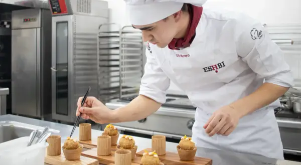Joven chef perfecciona pequeños bocados, demostrando su dominio en ciencias culinarias y gastronómicas.