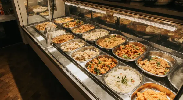 Variedad de platos calientes en un negocio de comida para llevar. Arroz blanco, pollo y guisos apetitosos listos para servir.