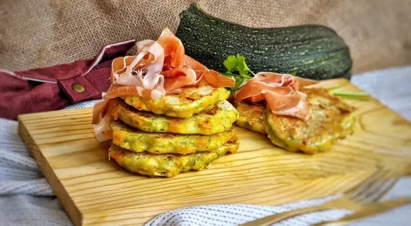 Deliciosas tortitas de calabacín apiladas y cubiertas con jamón serrano, listas para disfrutar.