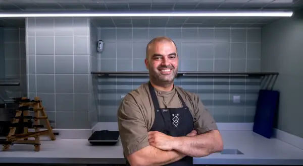 Chef sonriente con delantal negro en una cocina moderna, uno de los cocineros vascos famosos.