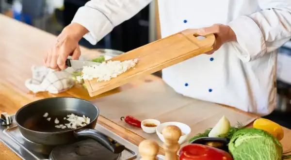 Un jefe de cocina, con su blanco uniforme, prepara cebolla picada para una sartén. Un convenio de sabor se inicia.