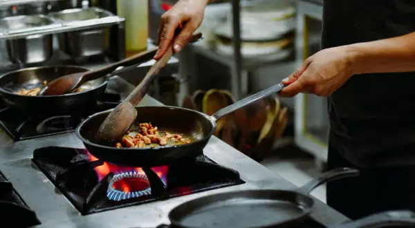 Manos expertas cocinan en sartenes sobre fuego vivo, un arte que se aprende en las mejores escuelas de cocina en España.