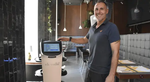 Un hombre sonriente junto a un robot que sirve comida en un restaurante moderno.