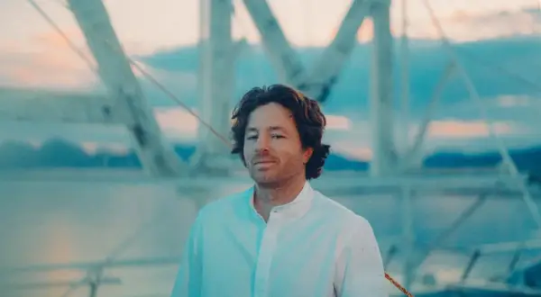 Jean Imbert, con camisa blanca, posa frente a una estructura de barco al atardecer.