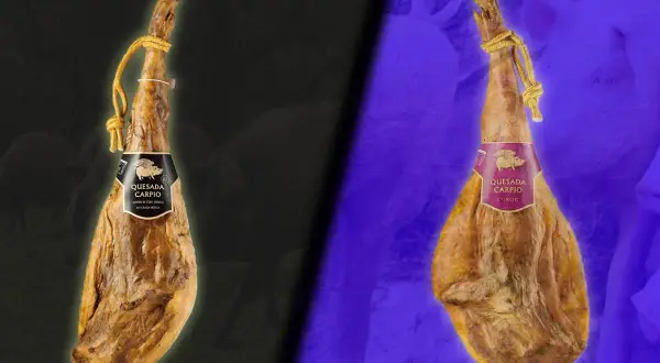 Dos jamones colgados, uno con etiqueta negra y otro con etiqueta morada, mostrando dos clases de jamón.
