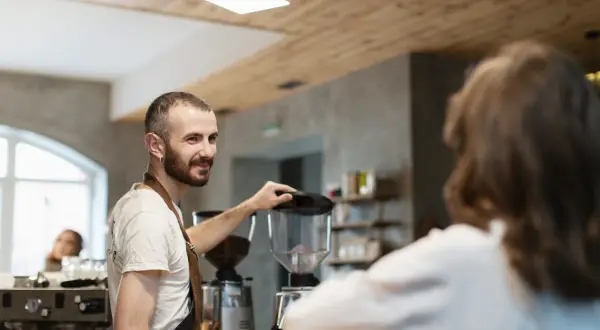 Barista sonríe mientras prepara café, un paso más para abrir su restaurante.