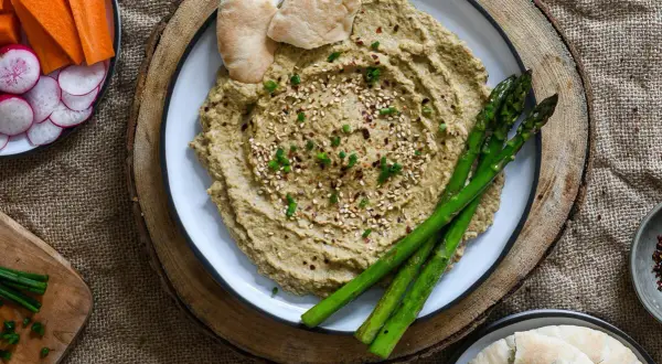 Hummus cremoso con espárragos, pan de pita y crudités de zanahoria y rábano. ¡Perfecto para tus ideas de picoteo saludables!