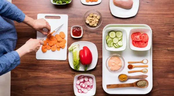 Mise en place restaurante: zanahorias cortadas, lechuga, pimiento rojo, pepino, tomate, pollo y condimentos listos para cocinar.