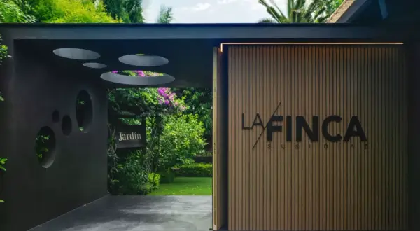 Entrada a "La Finca" de Susi Díaz, un jardín exuberante con un letrero de madera y una fachada moderna.