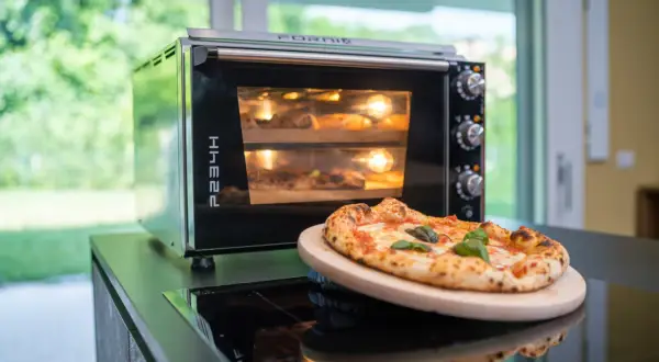 Horno eléctrico con dos pizzas dentro, una lista para disfrutar y otra en proceso. El tiempo de cocción de una pizza en horno eléctrico es clave para su textura.