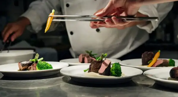 Chef emplata un plato de carne con brócoli y zanahoria, un detalle digno de una estrella verde Michelin.