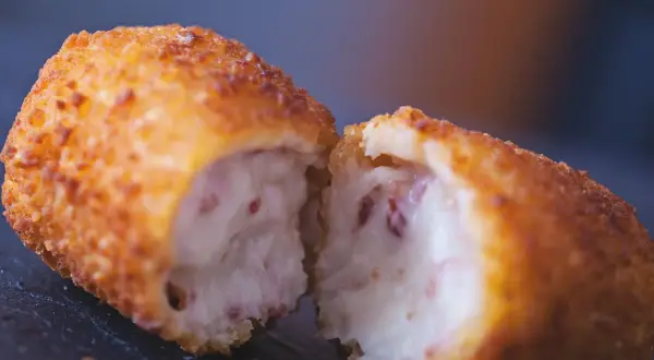 Croqueta dorada y crujiente, partida por la mitad, revelando un interior cremoso. La proporción de harina y leche para croquetas es clave para esta textura.