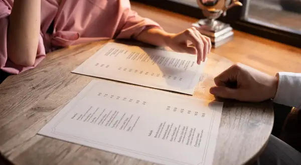 Pareja revisa el menú para decidir cómo hacer una carta de restaurante. Se ven platos como ensaladas y snacks.