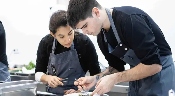 Dos aprendices de cocina, concentrados en emplatar un plato, aprendiendo como ser chef.