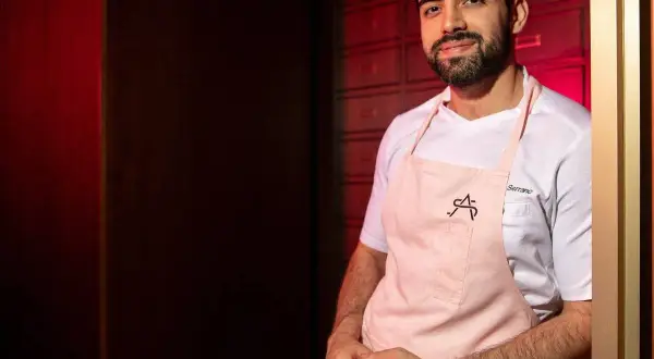 Chef Serrano, parte de la lista cocineros estrellas Michelin, sonríe con delantal rosa.