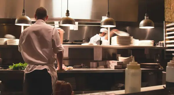 Un ayudante de cocina en España prepara ingredientes frescos en una cocina profesional, con pilas de platos y utensilios listos para el servicio.