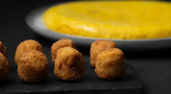 Croquetas doradas y crujientes, un ejemplo de que es la quinta gama hostelería, con una tortilla española al fondo.