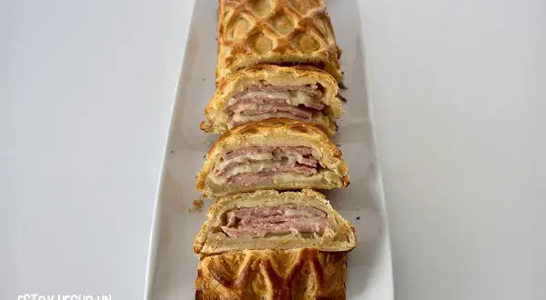 Delicioso hojaldre jamón york y queso al horno, cortado en porciones, con una capa crujiente y relleno jugoso.