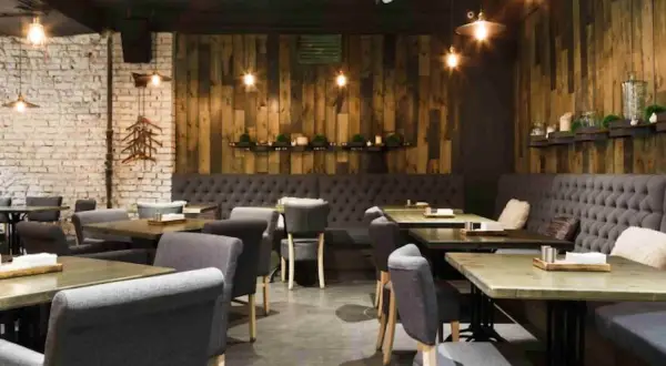 Interior de un restaurante de un tenedor con mesas de madera, sillas tapizadas y paredes de ladrillo y madera.