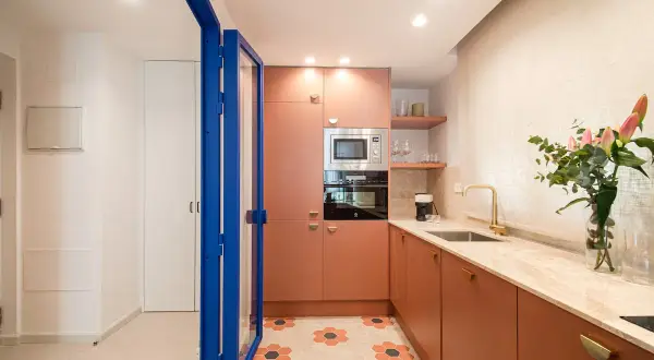 Cocina moderna con armarios naranjas, encimera de mármol y suelo hexagonal. Perfecta para un curso intensivo de cocina.
