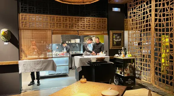 Chefs trabajan en la cocina de un restaurante. Se ve una mesa puesta y un carrito de bebidas. ¡Qué ganas de comer como Paco Méndez!