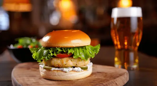 Deliciosa hamburguesa de pescado con lechuga, tomate y pepinillos, acompañada de una cerveza. ¿Cuánto tarda en descongelarse una hamburguesa?