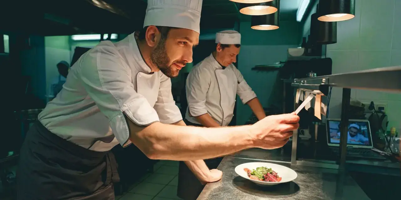 Un chef de partie, con su equipo, supervisa la preparación de un plato en una cocina profesional.