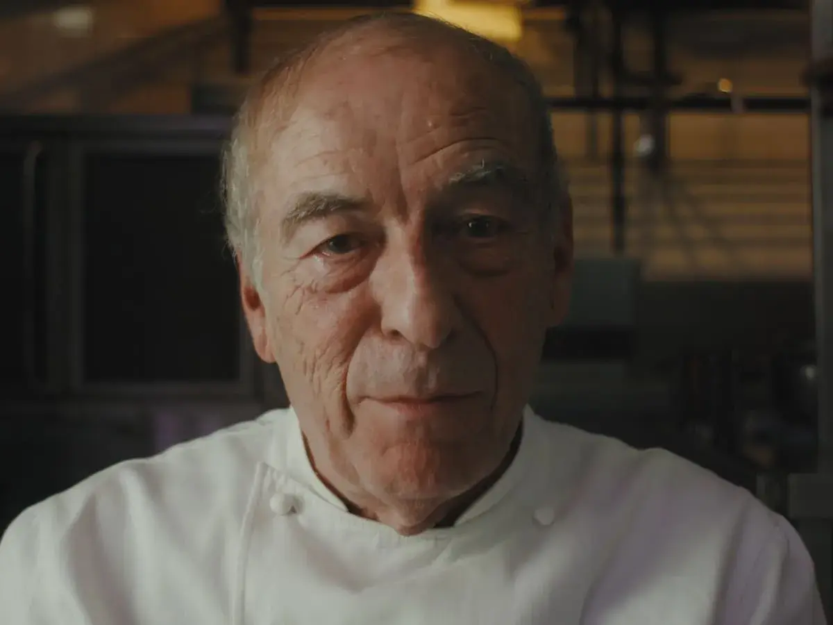 Retrato de un chef catalán con varias estrellas Michelin, con su uniforme blanco y mirada serena.
