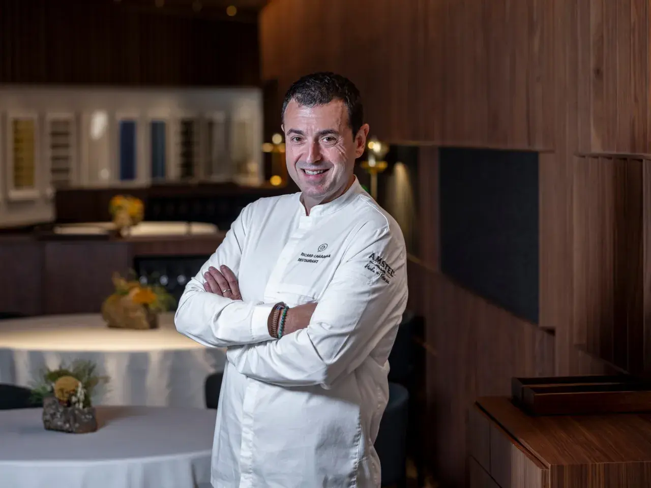 Chef sonriente en su cocina, con el logo de Ricard Camarena Restaurantes en su uniforme.