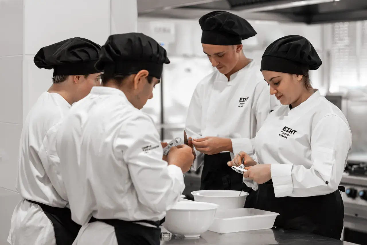 Estudiantes en cursos de cocina para profesionales, concentrados en sus tareas en una cocina profesional.