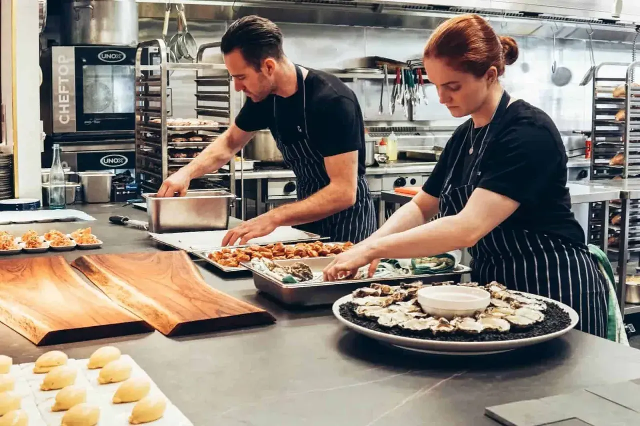 Dos cocineros preparan platos en una cocina profesional. ¿Cuánto gana un cocinero en Australia?