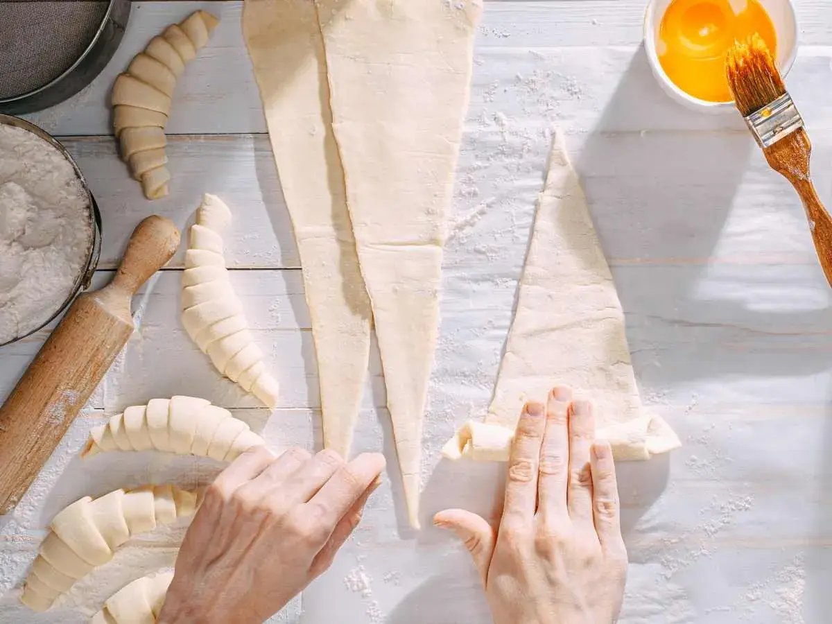 Manos enrollando masa para croissants. ¡Se pueden congelar los croissants para hornearlos más tarde!
