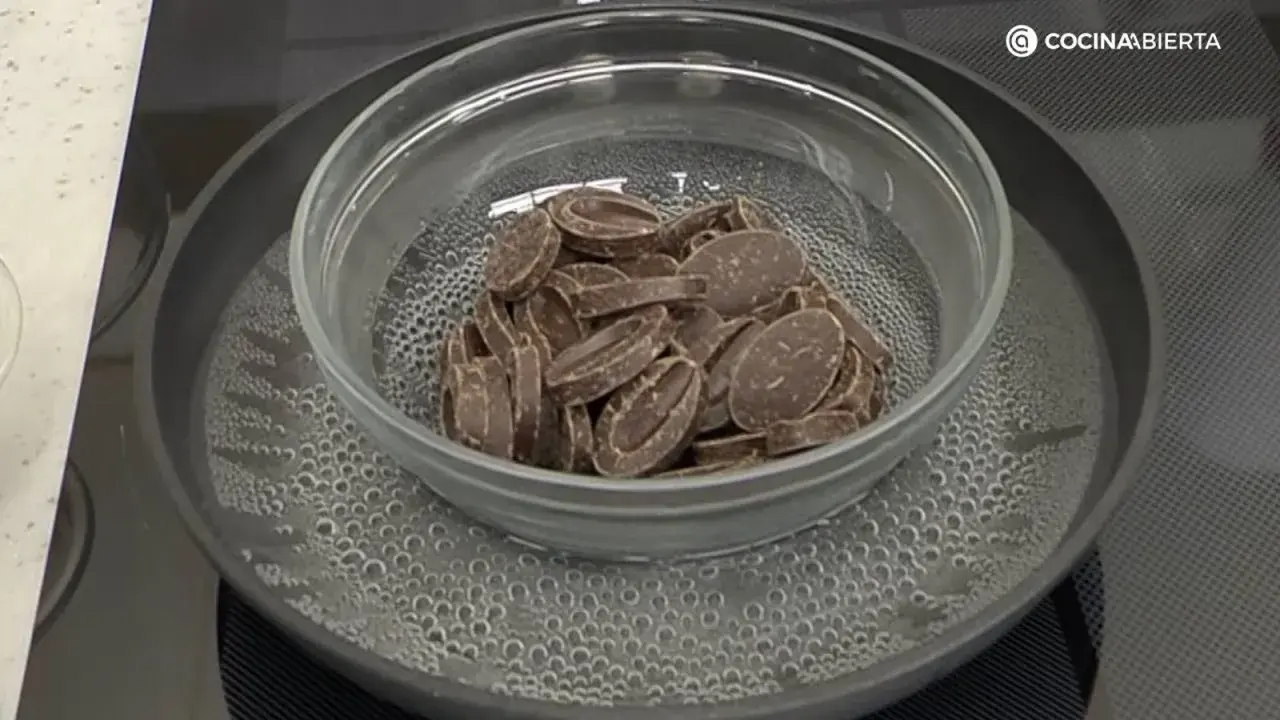 Chocolate troceado derritiéndose suavemente en un bol de cristal sobre un baño maría hirviendo.