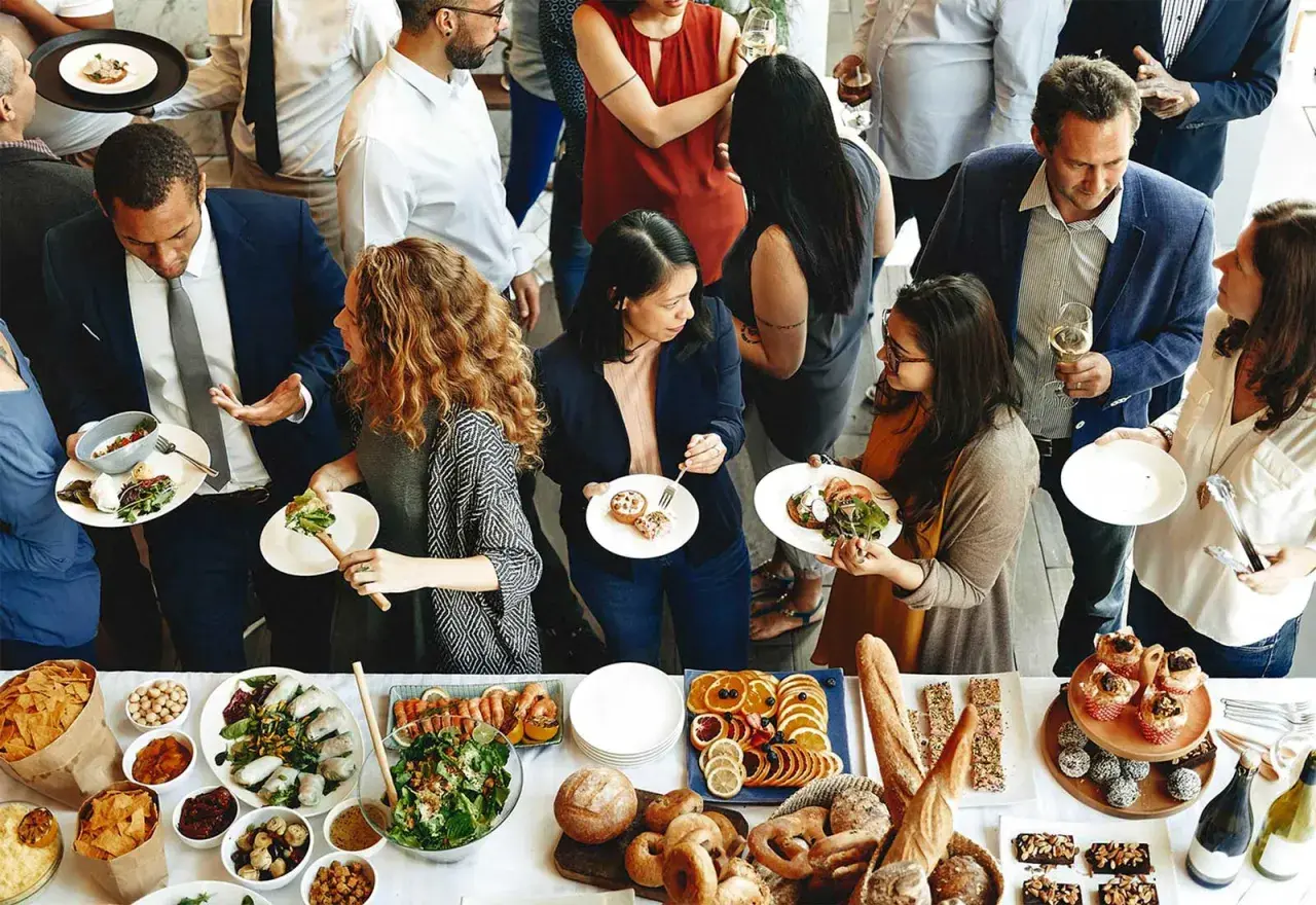 Gente disfrutando de la comida de personal en restaurantes, con una mesa llena de ensaladas, mariscos, frutas y pan.